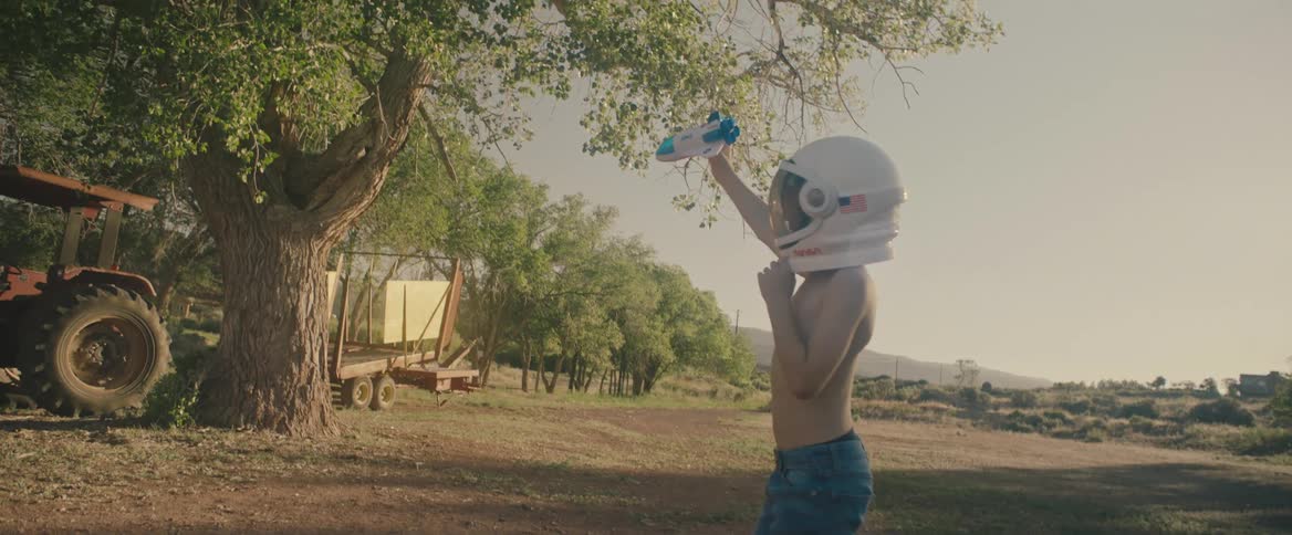 Young shirtless boy wearing a toy astronaut helmet playing with a space shuttle toy outdoors