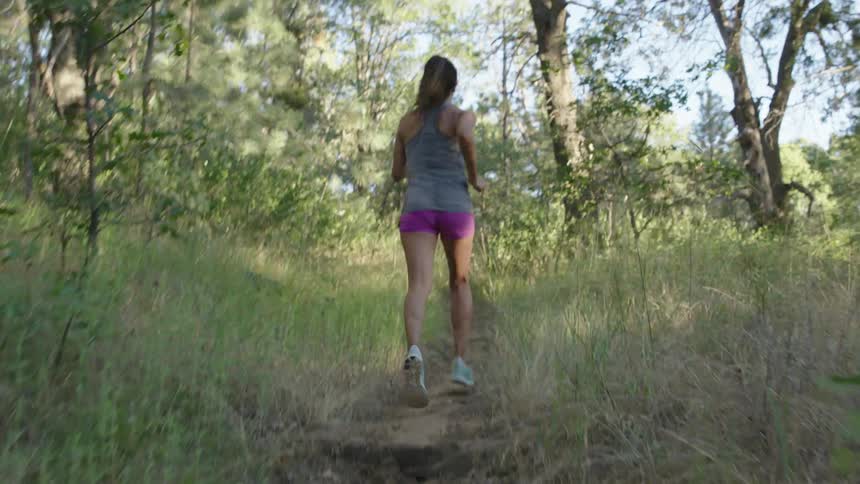 A woman jogs on a narrow dirt path in a wooded area
