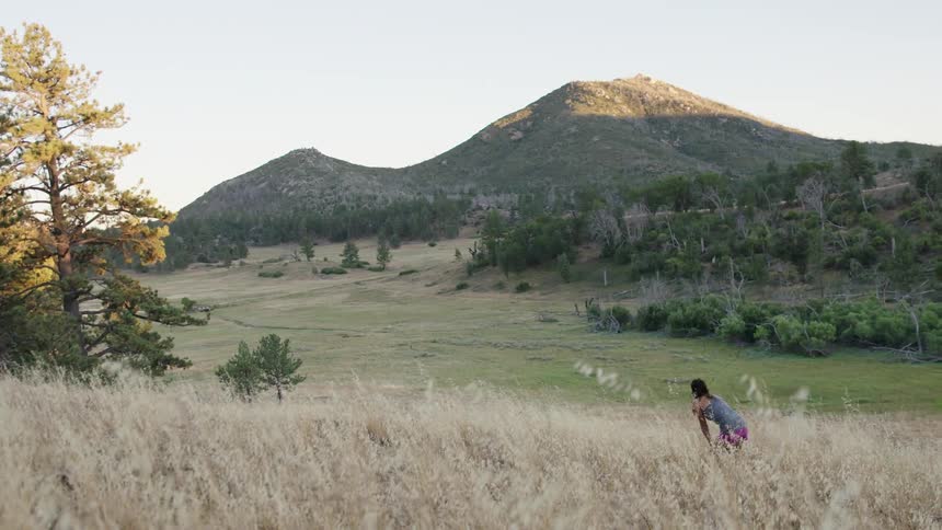 A woman runs in some tall yellow grass before resting