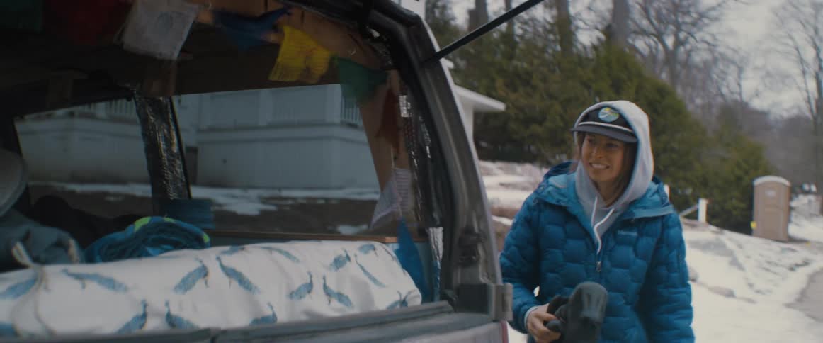 A woman closes the car door and walks to the back to load her booties in with the other surf gear