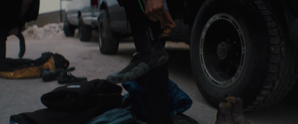 A man and woman standing in a parking lot pulling on their wet suits and booties