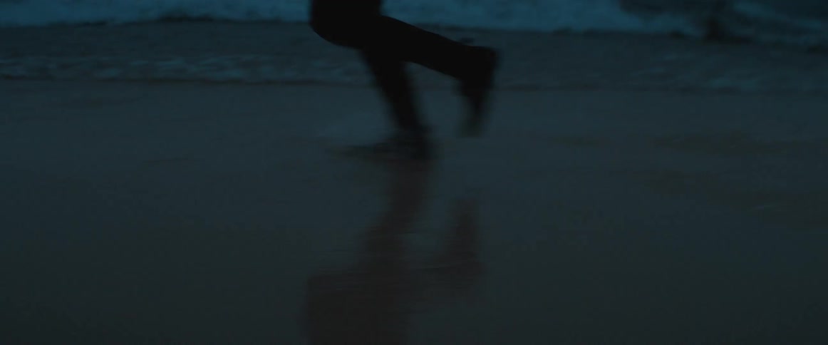 A person running along the beach runs through waves rolling in to the shore