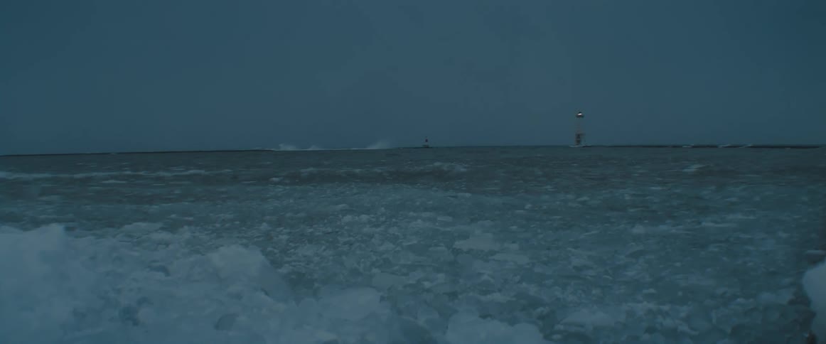 Lighthouse in the horizon in front of a frozen beach near the ocean at evening