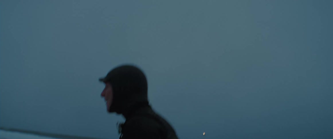 A man is walking on the coast of a beach at dusk