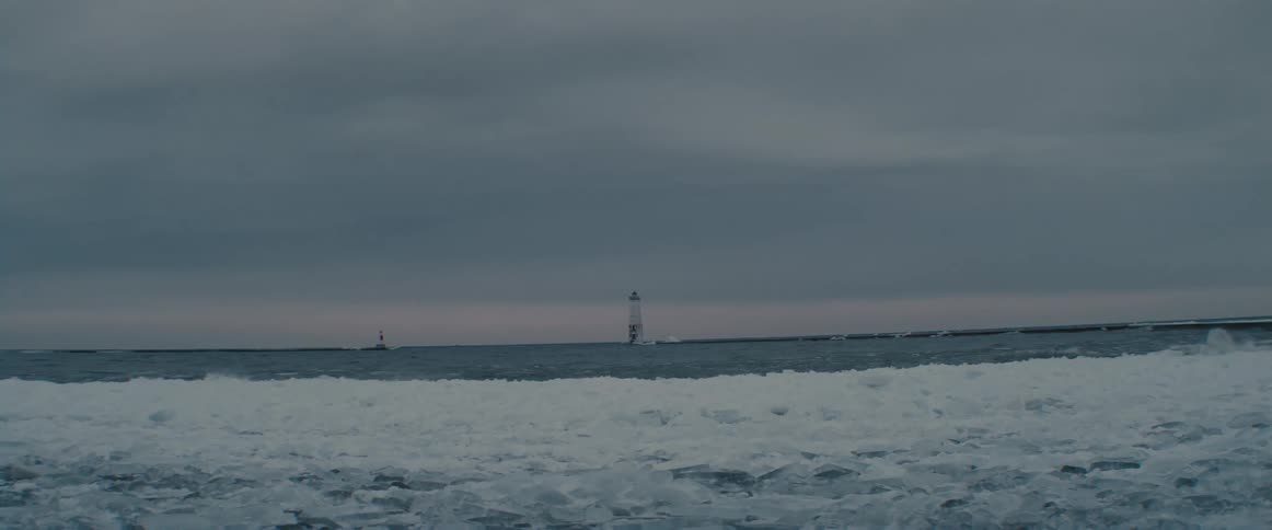 Lighthouse in the horizon in front of a frozen beach close to the ocean at sunset