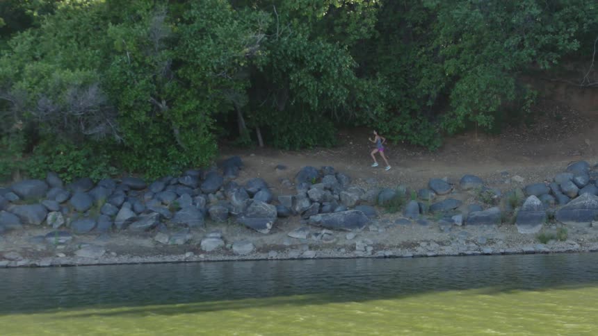 A woman jogging through a wooded area next to a lake
