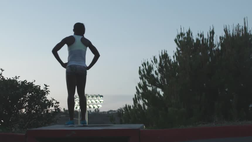 A female athlete steps up onto a vacant podium at dusk