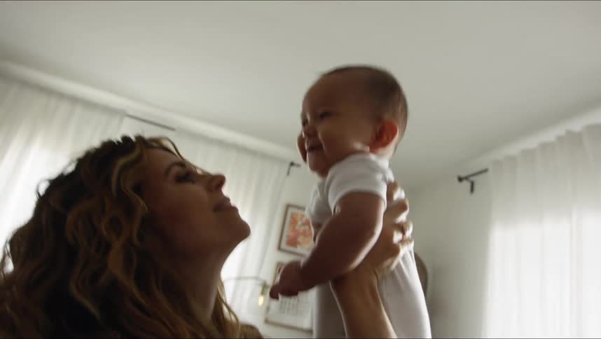 Baby laughs as mom lifts him up then hugs and kisses him