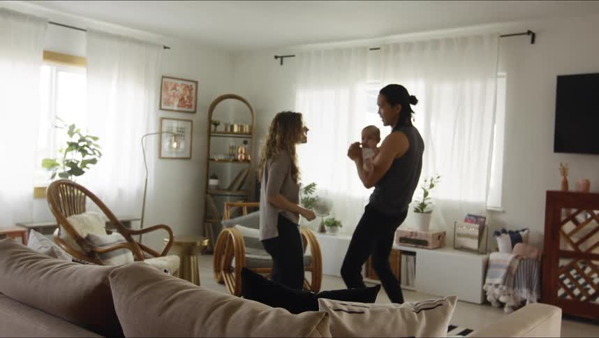 A man and woman dance around their living room with their baby