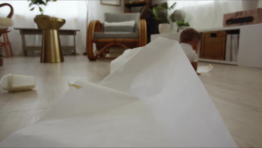 A baby crawls underneath an unfurled roll of paper