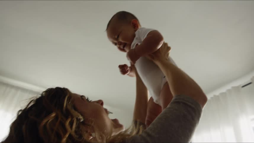 Mother holds baby in air smiling then crouches quickly while cradling child