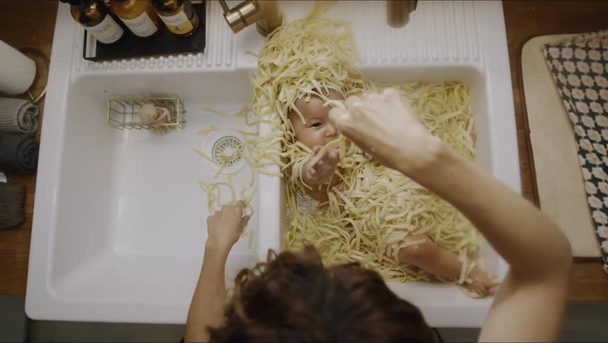 A woman plays with her baby as hes immersed in a sink full of pasta