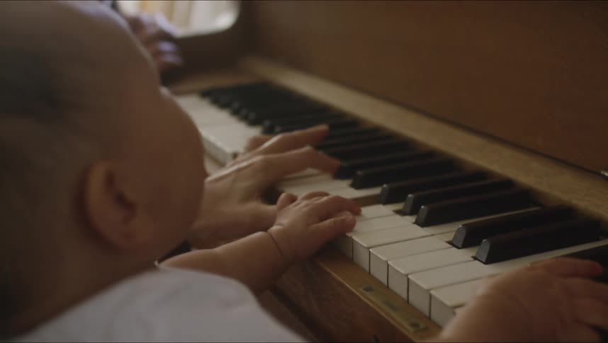 Mother holds baby son and plays piano together