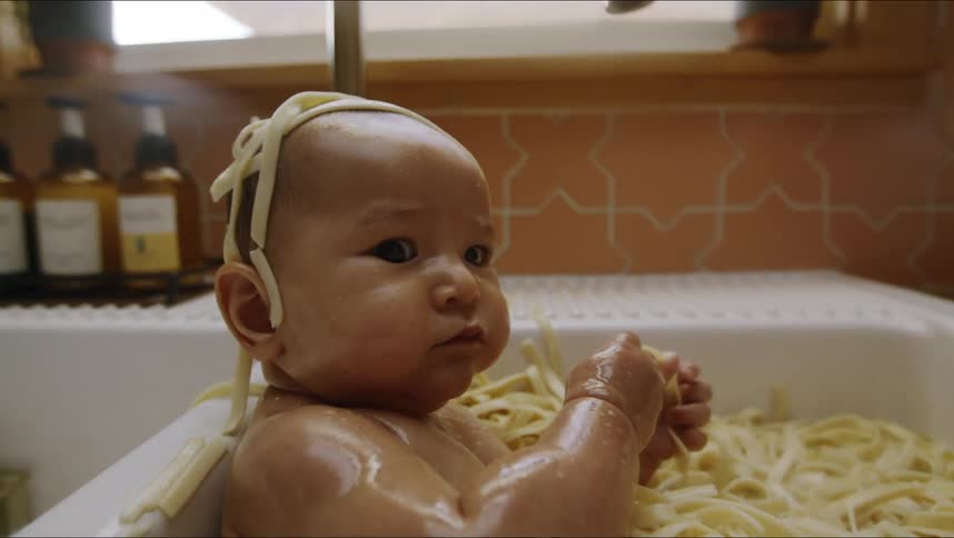 Baby sits in kitchen sink full of noodles eating
