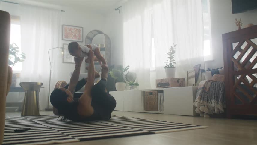 A man lies on the floor and lifts his son up with his feet