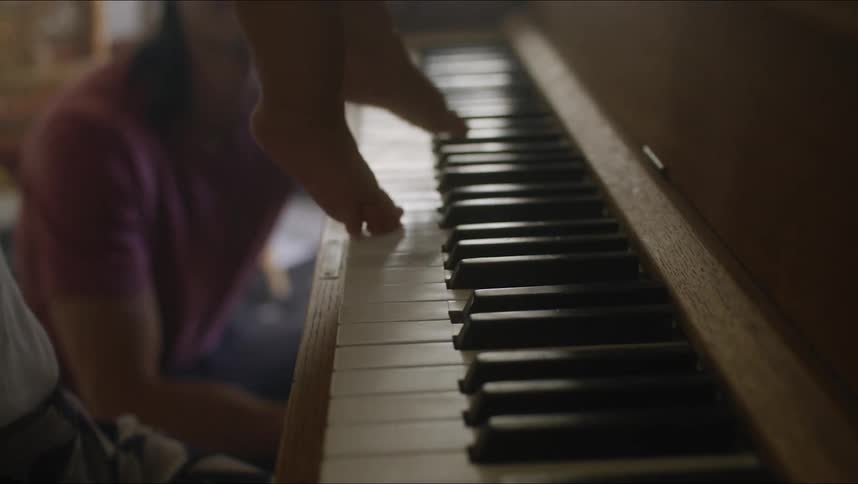 Woman holds a baby over the piano keys while another woman watches