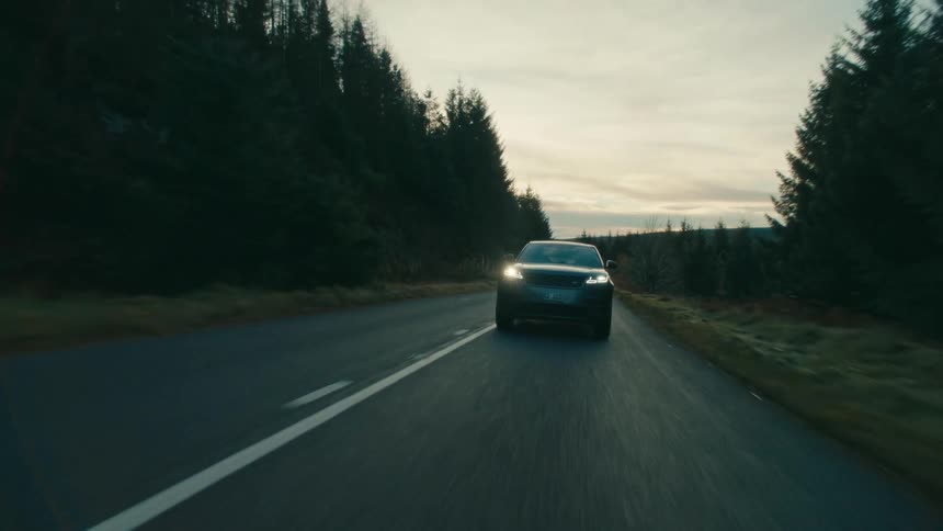 An automobile is traveling on a forest road with the headlights on