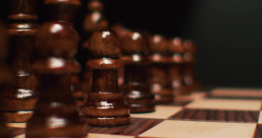Brown wooden chess pieces lined up on a chess board