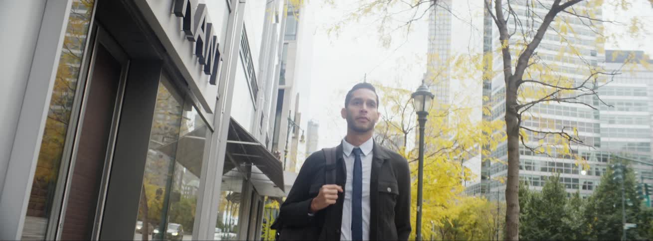 Young professional with backpack walking on city sidewalk commuting to work