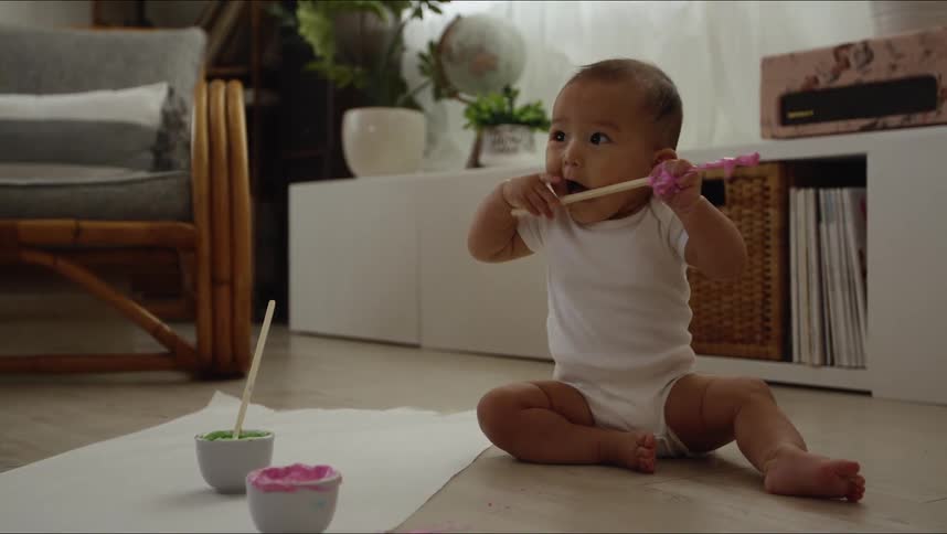 A small infant sits on the floor and plays with a colorful stick