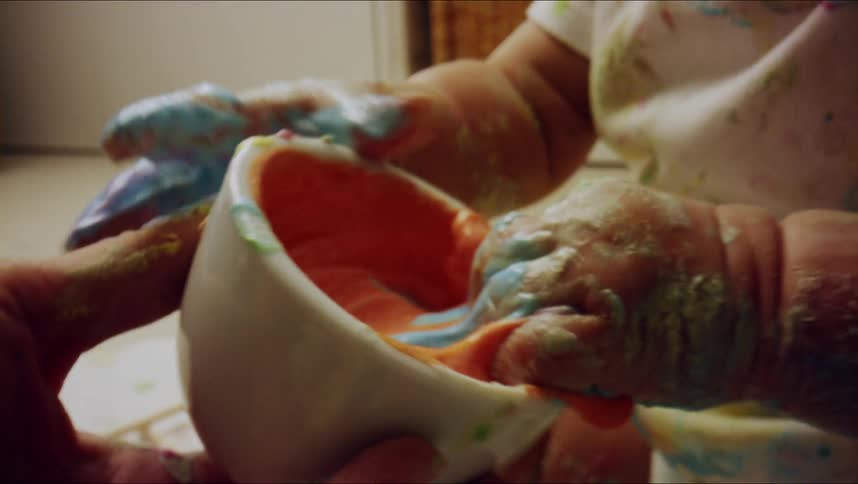 Baby plays with colored paste getting it all over their face and hands