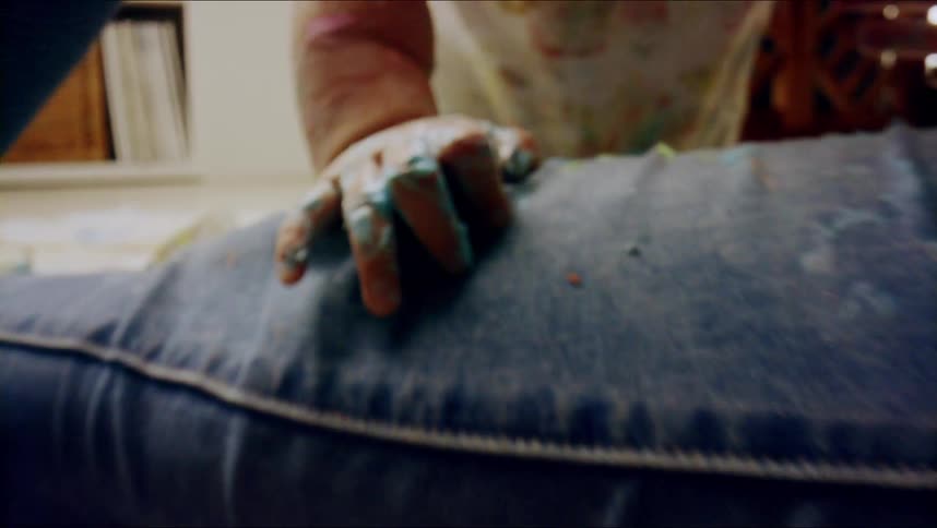 A babys paint covered fingers grasping moms leg