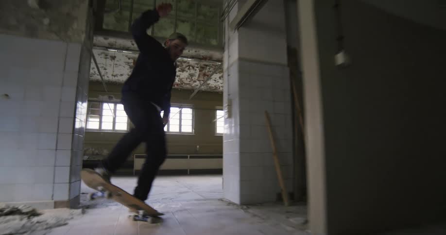 Man rides a skateboard through an empty dilapidated building