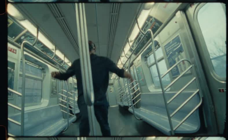A man dances and hangs from inside an empty train car as it passes through a city