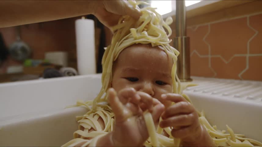 A mother is bathing her baby in linguine