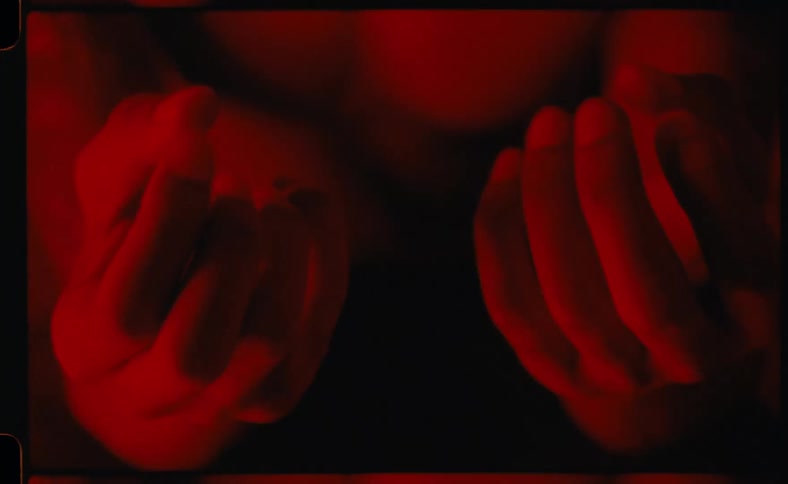 Shirtless man under a flashing red light clenching his fist and moving his fingers
