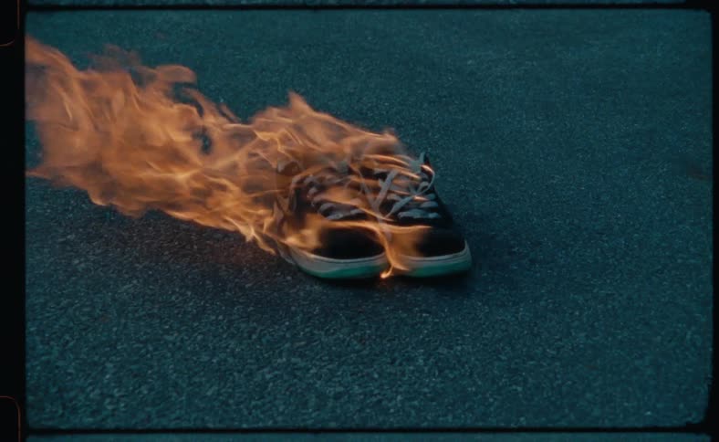 A pair of tennis shoes sitting on concrete are engulfed in flames