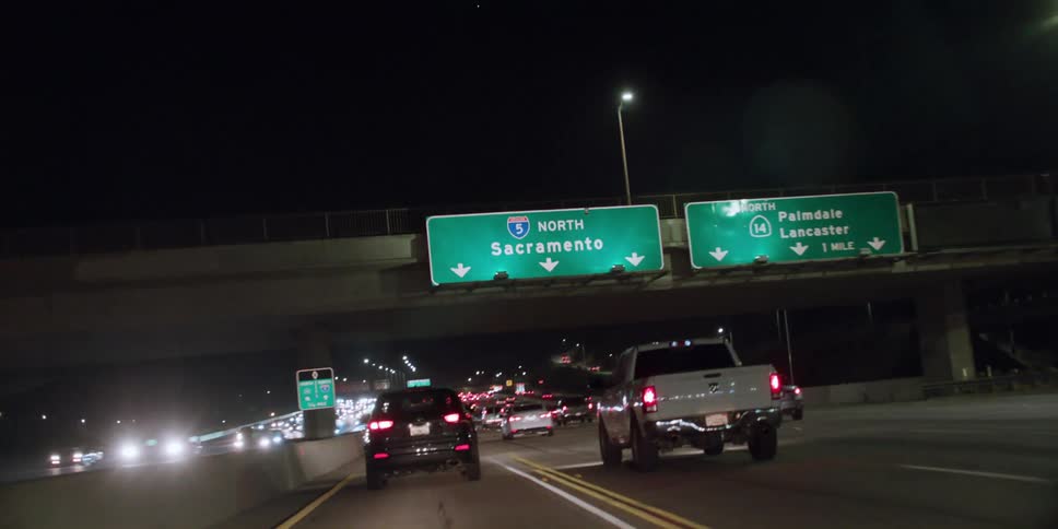 Cars and trucks travel on a highway at night in busy traffic