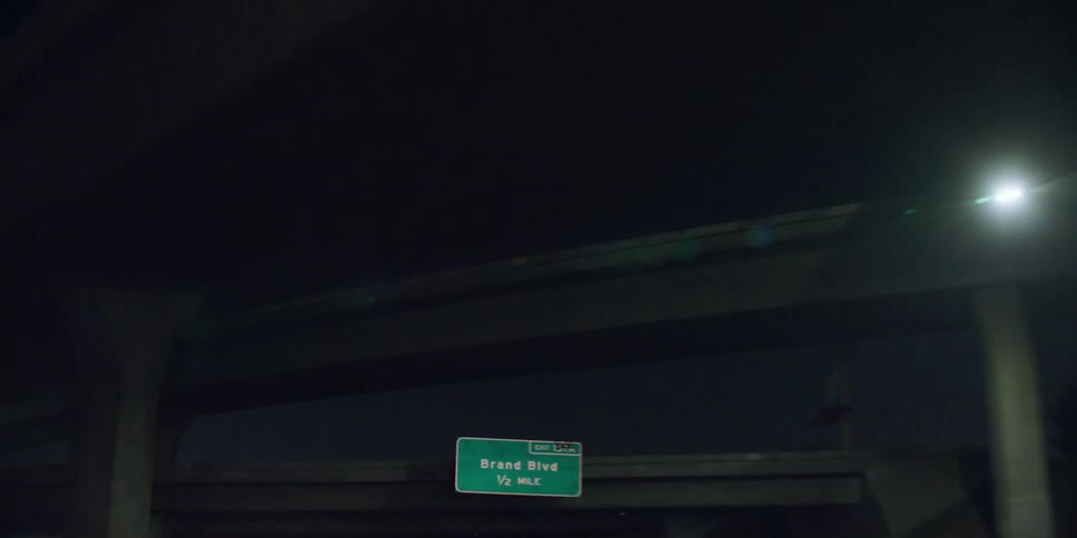Automobiles are traveling on a highway and through an overpass at night