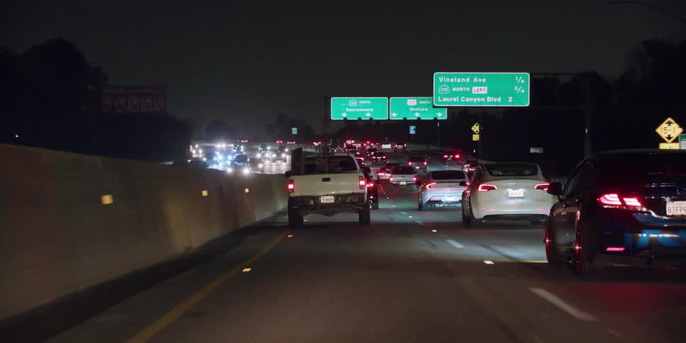 Cars and trucks travel on a highway at night in busy traffic