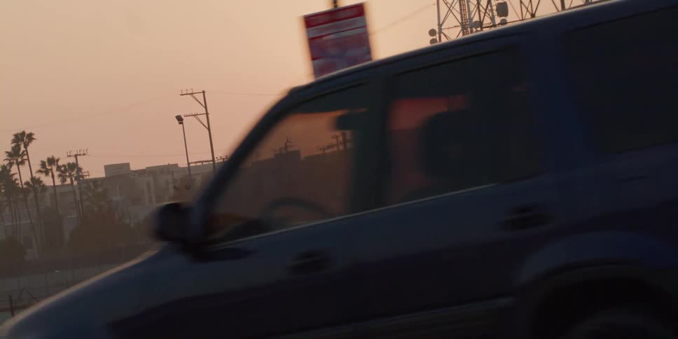 The sun is rising above buildings near transmission towers as traffic moves through town