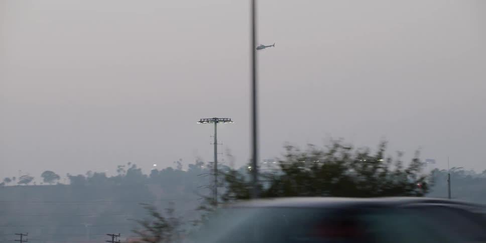 Traffic moves by as a helicopter flies high in the sky over trees and utility towers