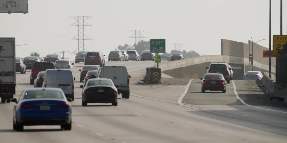 Automobiles are traveling on a highway and through an overpass and utility towers are in the distance