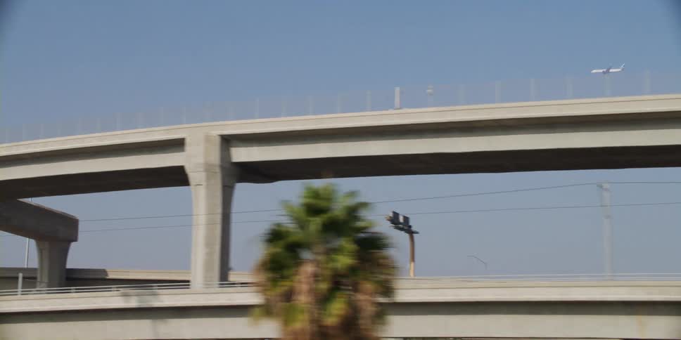 Vehicles travel on a cement bridge as a jet flies overhead