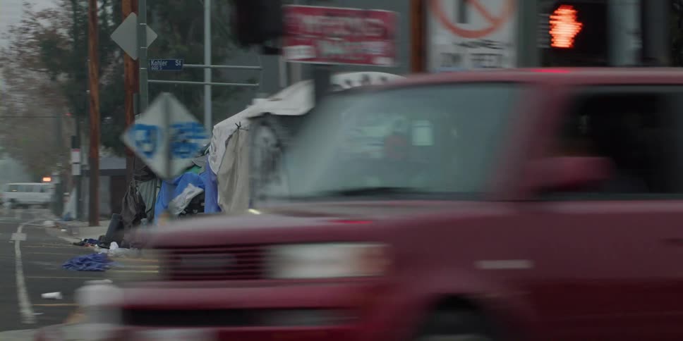 Man stands near corner with tent shelters sits on sidewalk outside fence surrounding a building