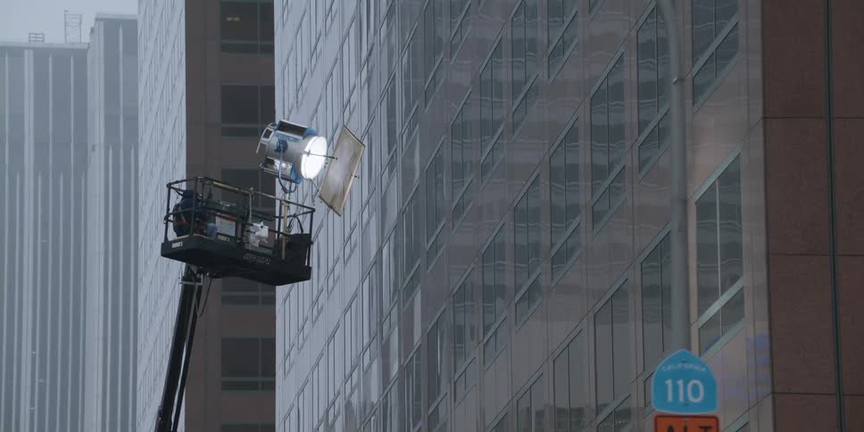 A filmmaker knees on a platform outside a high rise office building as they film