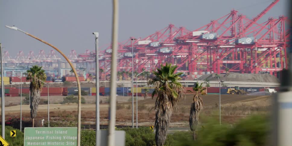 Vehicle passes on highway as bulldozer and spraying truck move near waterfront loading dock