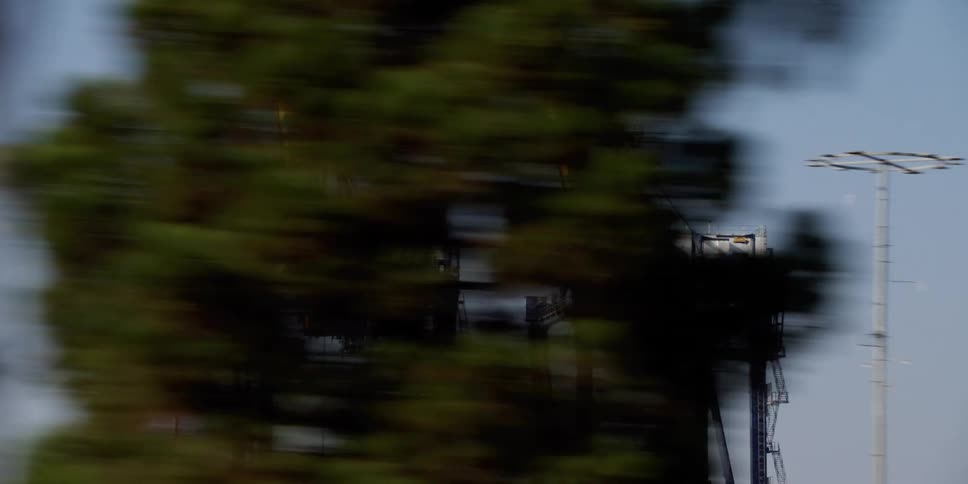 Train travels between the trees and two pieces of machinery