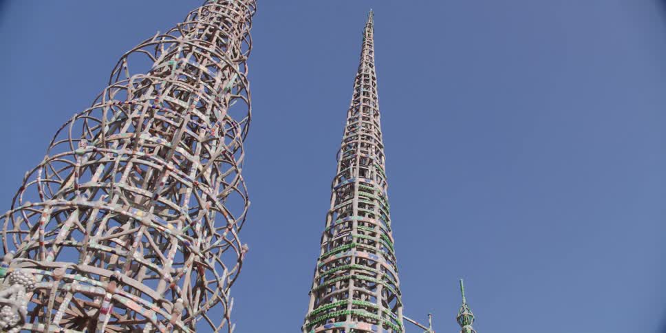 Looking up at two tall metallic spires in a park on a cloudless day