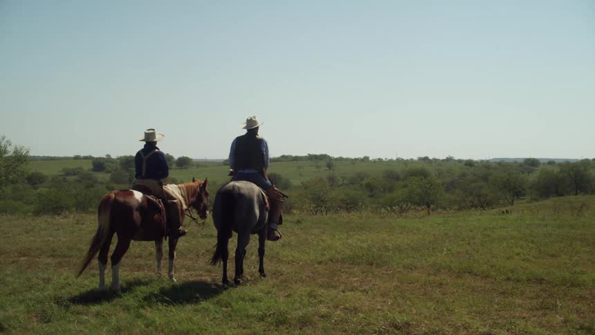 Two men on horseback on a pasture looking out into the distance