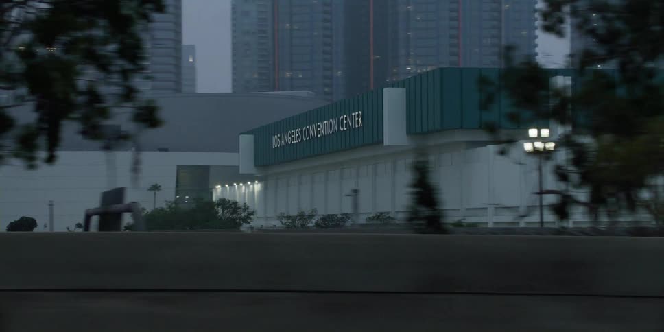 Exterior view of los angeles convention center with high rise buildings in the background seen from moving car on highway