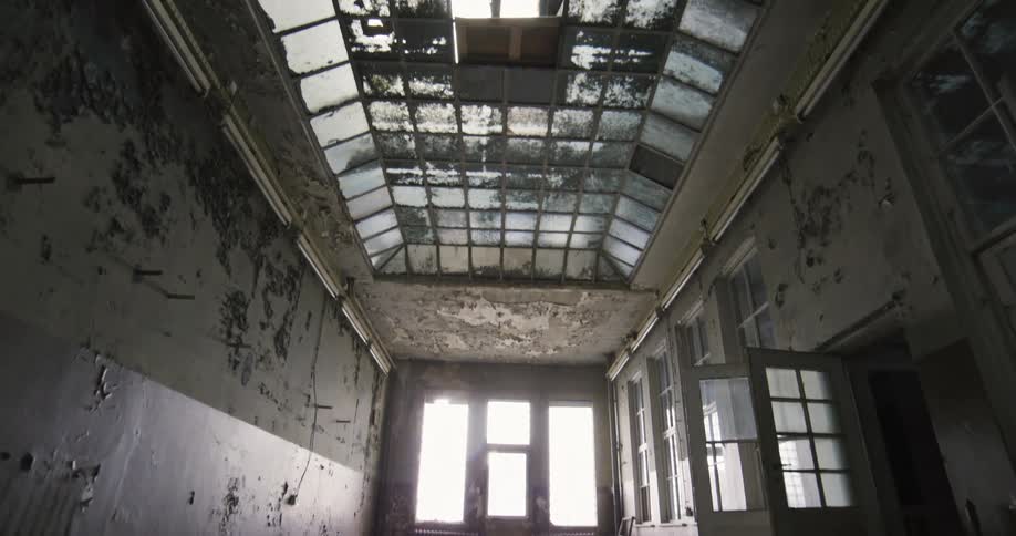 Person stands to side of drop cloth covered room with a glass ceiling and peeling wall paint