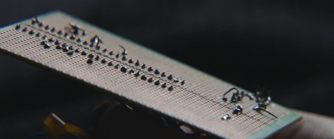 A hand tilts a panel with holes and black pieces back and forth