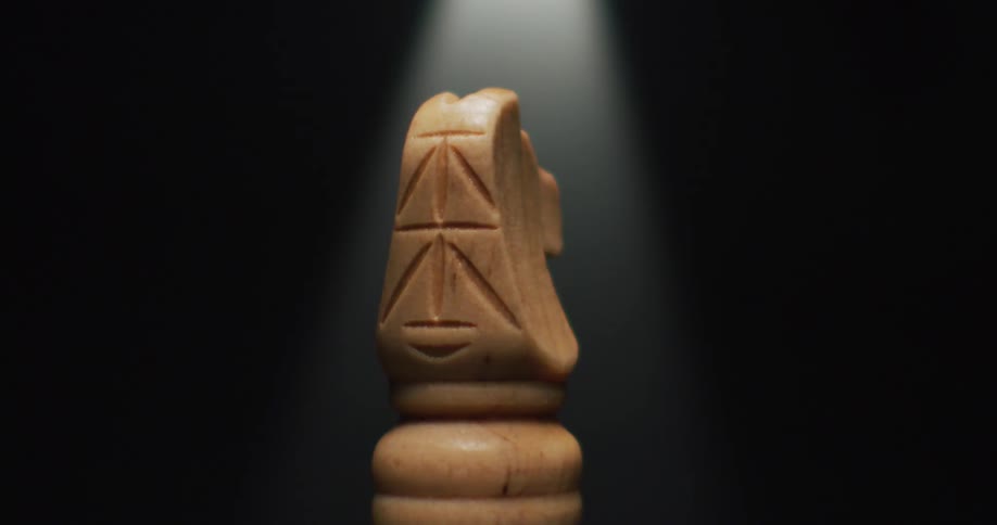 Carved stone knight chess piece stands in dark area under a light