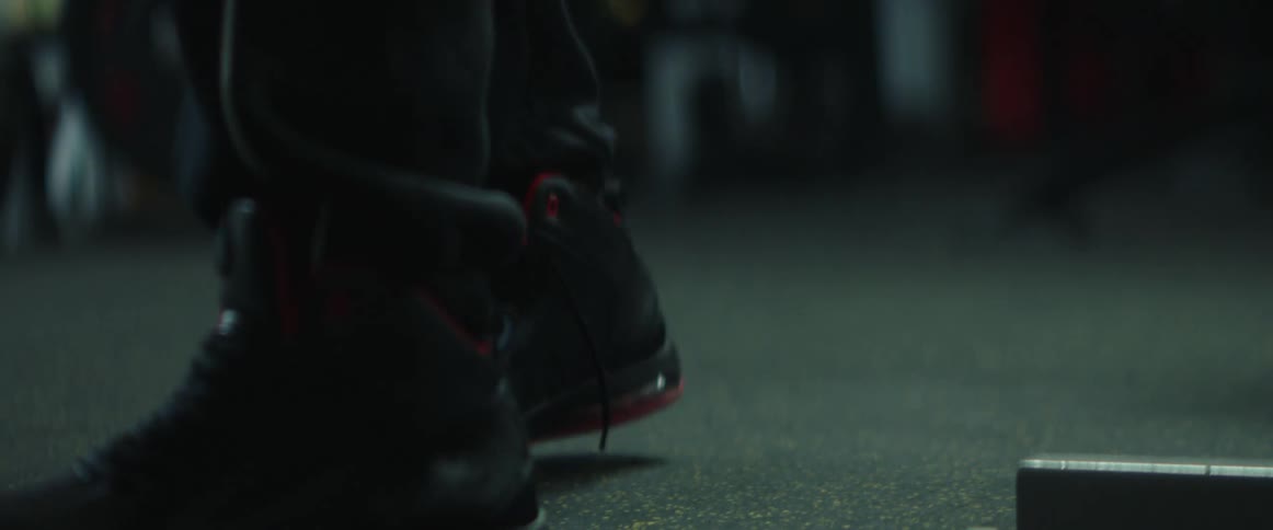 A person wearing black shoes and black pants walking inside an empty gym