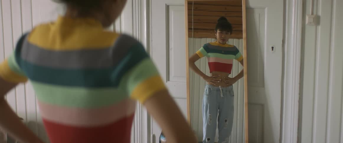 Asian woman looks at herself in a mirror and squeezes her bare tummy with her hands